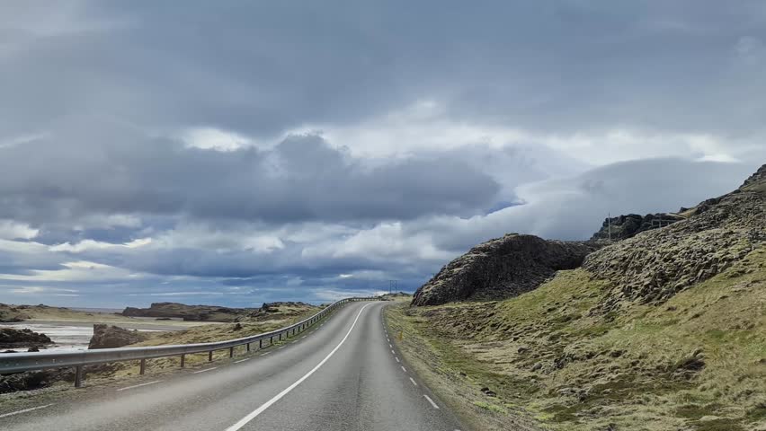 Point of view driving on a winding asphalt road through the rugged and mossy landscape of Iceland