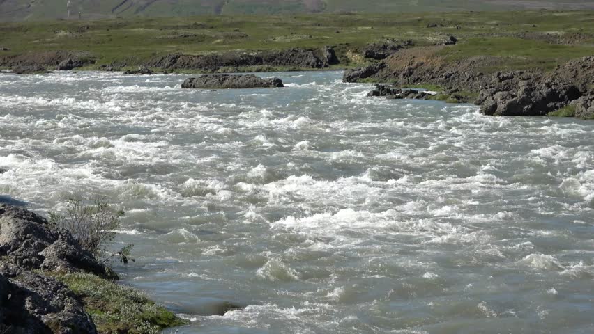 White water rapids of a wide river flowing through a wild and rocky Icelandic valley in summer