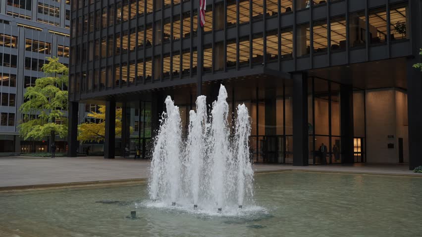 City Plaza Fountain At Dusk, Water Jets Rise From Reflective Pool In Front Of Modern Glass Office Building, Illuminated Windows And Warm
