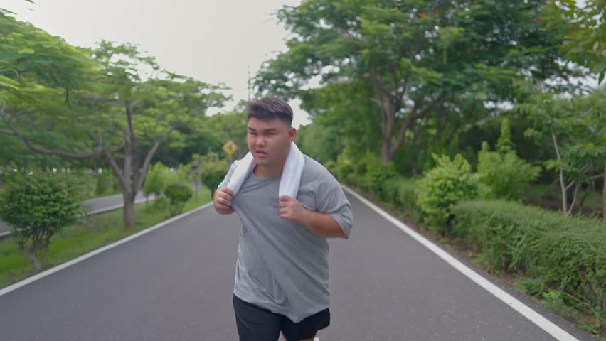 Asian plus-size man exercises outdoors in the garden to lose weight. Attractive young overweight guy spend leisure time on weekend doing running workout to improve health and overall fitness in park.
