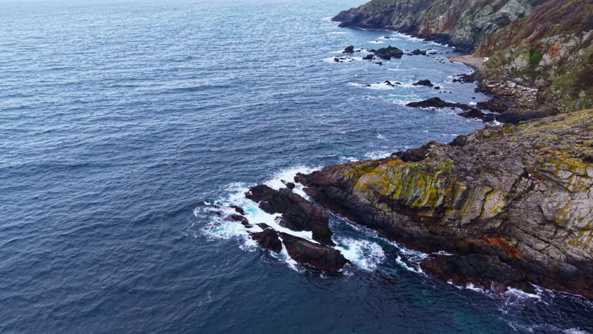 Waves roll gently over the rocky shore as the early morning light casts a soft glow over the landscape. Seabirds glide above the peaceful waters, creating a serene atmosphere.