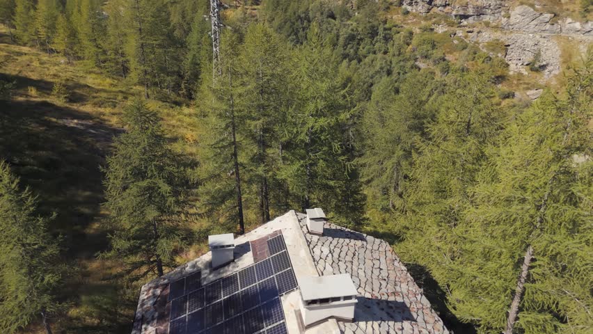 Aerial panning right of a hotel surrounded by tall pine trees in Italy, Aosta Valley, Valle d’Aosta, showing the alpine landscape