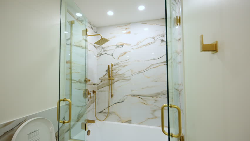 Luxury bathroom featuring a glass-enclosed shower with elegant gold fixtures. The marble-style wall tile adds a high-end, sophisticated look.