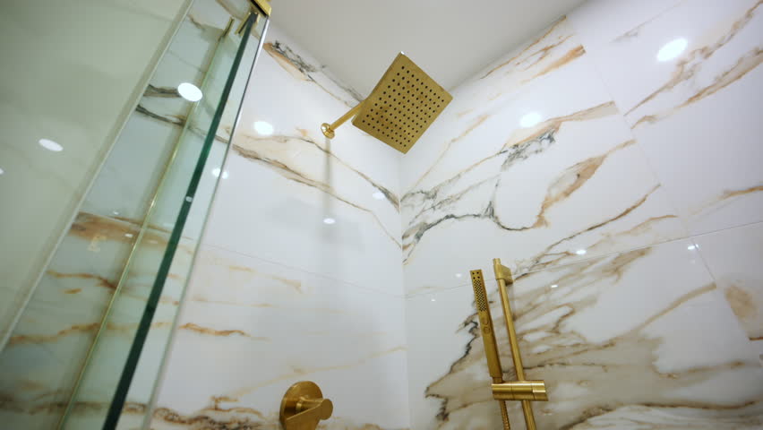 Luxury bathroom shower with elegant gold fixtures. The marble-style wall tile adds a high-end, sophisticated look.