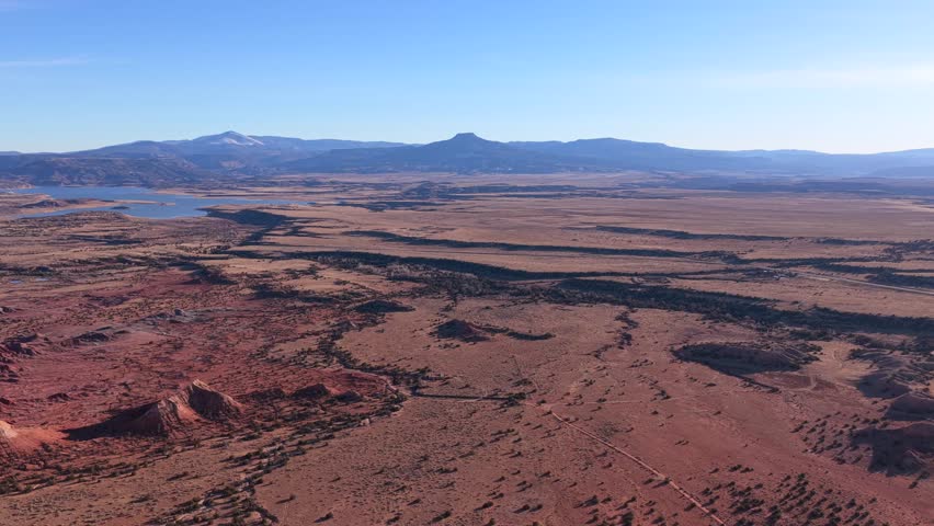 Drone footage moves steadily across expansive desert plains toward Cerro Pedernal, revealing winding land patterns, sparse vegetation, distant water, and layered terrain beneath clear blue skies.