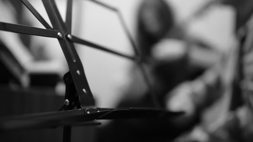 Cinematic black and white close-up of piano, guitar, and music stand. Student with guitar and teacher softly defocused. Captures the intimate, artistic atmosphere of a music lesson.