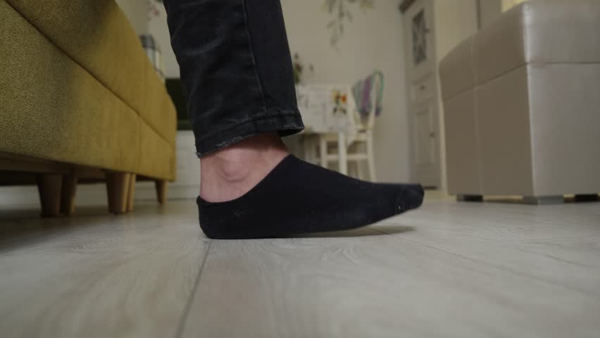 Close up low angle view of foot in black sock stepping and stomping on light wood laminate floor near yellow sofa. Indoor home scene with casual movement.