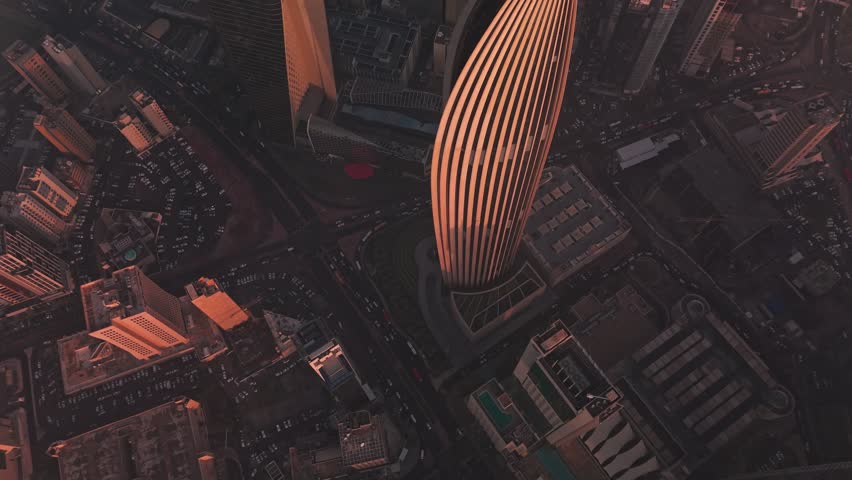 Top down drone of a curved ribbed landmark tower in Kuwait City at golden hour. Traffic and roads create graphic patterns. Ideal for corporate travel real estate and establishing shots.