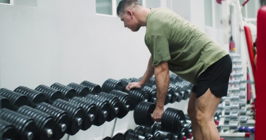 A middle aged Caucasian man working out in the gym. Workout with big dumbbell for back muscles. Physical education as a norm of life for maintaining health. Slow motion 4k footage.