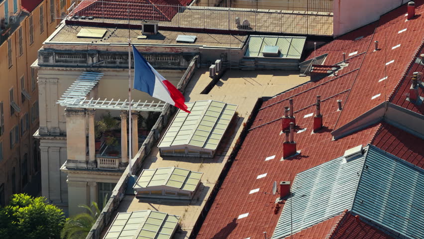 Aerial drone view of a French flag waving above a historic building in central Nice, with rooftops in the background