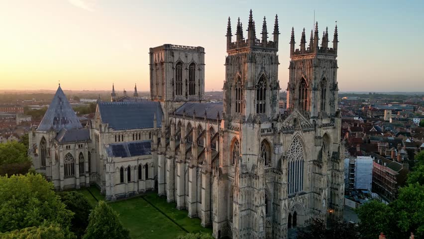 Aerial drone point of interest counter clockwise around the main entrance of York Minster, gradually revealing the sunrise and early morning light over the Gothic cathedral in York, England.