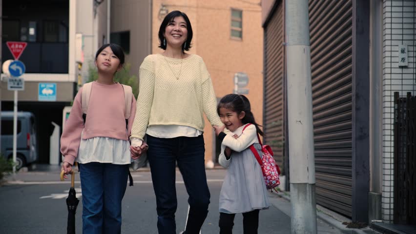 Happy Asian family with a mother and two daughters holding hands and walking together in the city