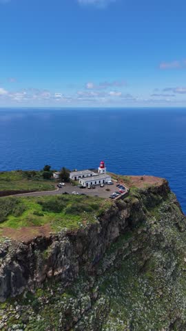 Aerial 4K drone footage of dramatic coastal cliffs and lighthouse viewpoint on Madeira island, overlooking the deep blue Atlantic Ocean and rugged shoreline in clear daylight.