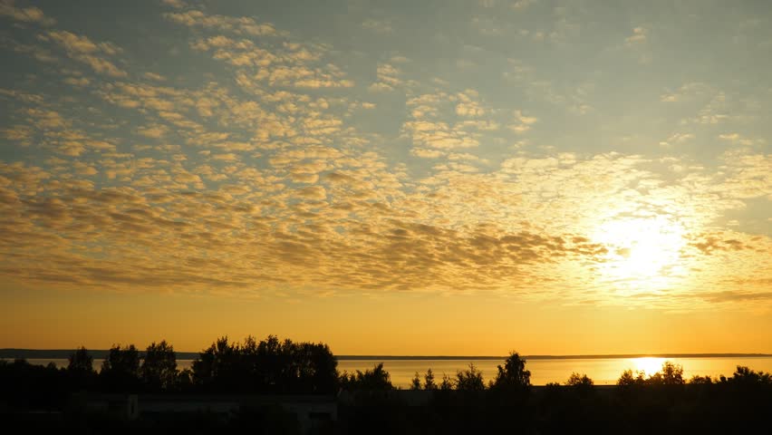 Breathtaking yellow golden clouds and sunrise over Onega Lake, showcasing the sun ascent across the morning sky, illuminating the tranquil shores and vibrant reflections, welcoming new summer day.