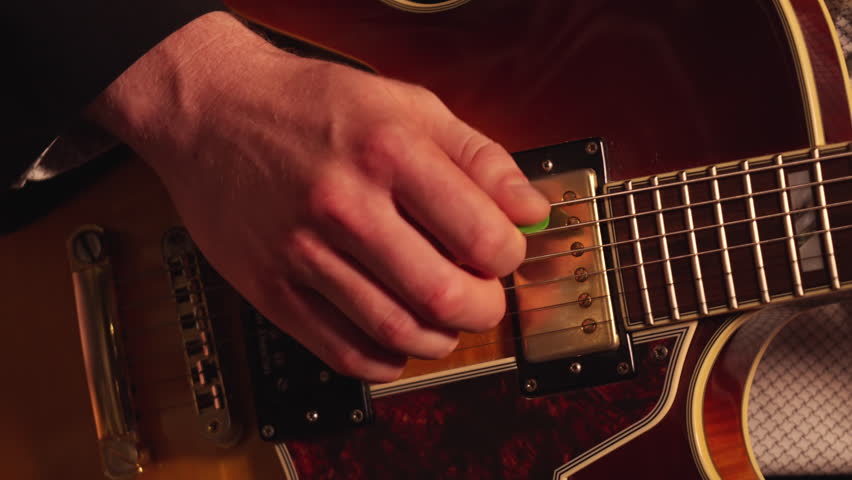 Person playing a guitar with a pick, close up