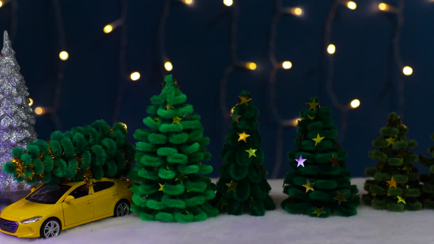 On a dark blue background with flashing lights among many green Christmas trees, there is an orange-blue house and a yellow car