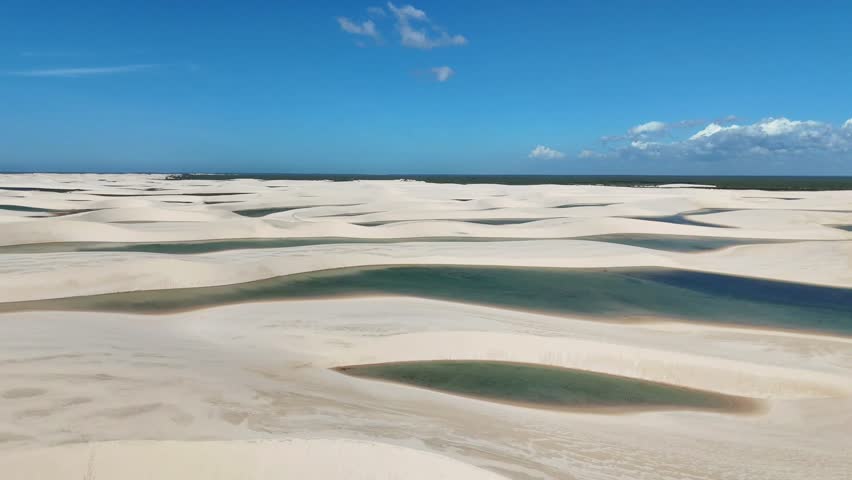 Aerial drone view descending over the unique white sand dunes and blue lagoons of Lençóis Maranhenses National Park, Brazil.