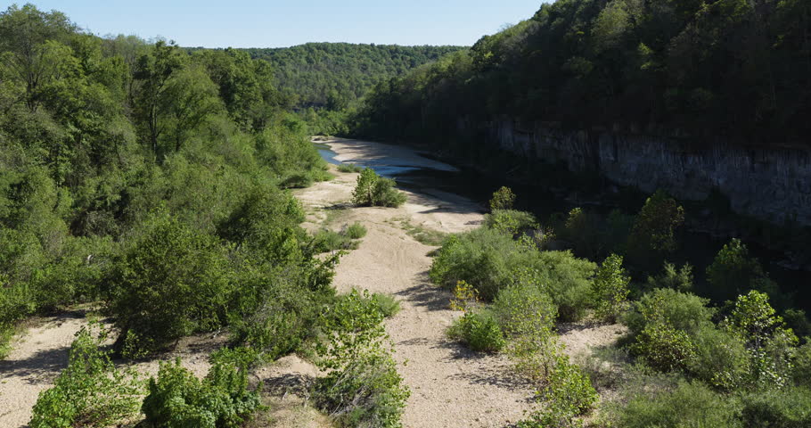 River cutting through steep wooded bluffs in warm autumn light with winding water and deep shadows, aerial pullback