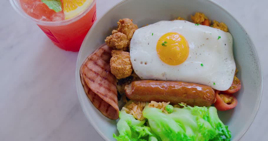 Hearty breakfast bowl with sunny-side up egg, grilled ham, sausage, rice, and fresh lettuce. Delicious brunch meal, comfort food concept. Bright, inviting lighting.
