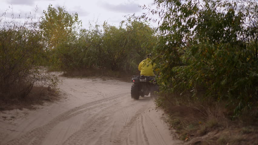 Yellow jacket rider navigates winding dunes, twoquad convoy threading leafy scrub corridors and soft sand tracks under overcast sky, steady pace and scenic