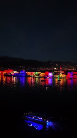 Drone footage of colorful Christmas light projections illuminating the entire Isola dei Pescatori on Lake Maggiore at night, creating a magical festive atmosphere in Piedmont, Italy