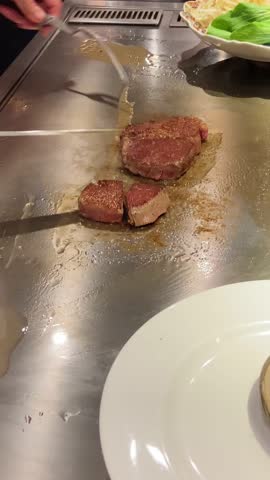 Japanese grill gourmet restaurant as chef cooks high quality meat. Using knife and fork to slice piece of premium Kobe beef marbled meat. Traditional teppanyaki style hot plate grill. UGC foodie vlog