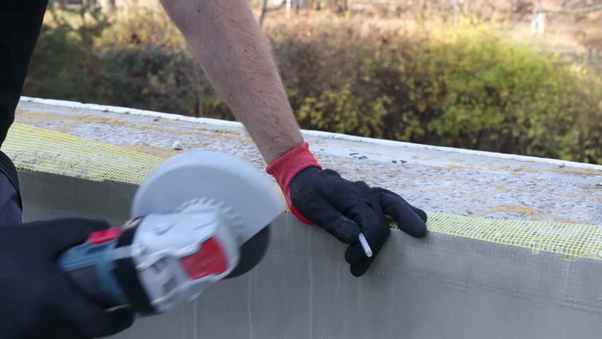 Close-up of a construction worker using an angle grinder to cut concrete during exterior renovation. Bright sparks fly while professional handyman works with power tools on a construction site. Concept of construction industry, repair work, building renovation, safety, manual labor and industrial tools
