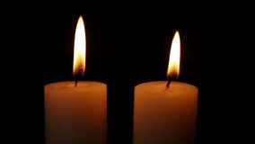 Two lit candles stand close together in a dark setting as their flames flicker gently with small rhythmic movements creating a steady warm glow throughout the scene - Powered by Shutterstock - Get 15% off with code: PIKWIZARD15