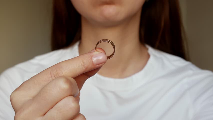 
A broken heart after betrayal. A woman holds a wedding ring, a painful process of letting go.