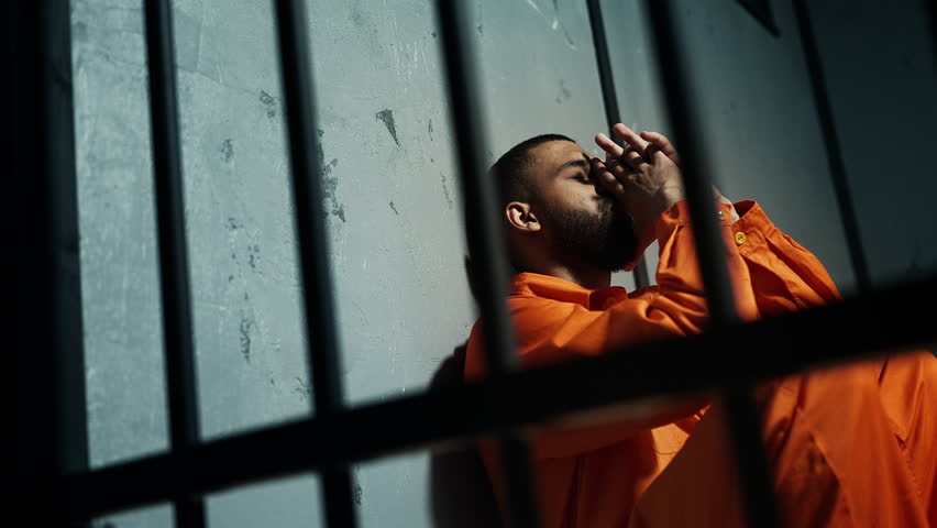 African American inmate sitting on floor behind bars, feeling regret and remorse