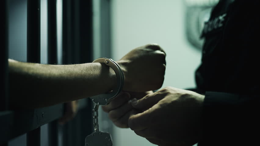 Police officer removing handcuffs from inmate standing behind jail bars, arrest