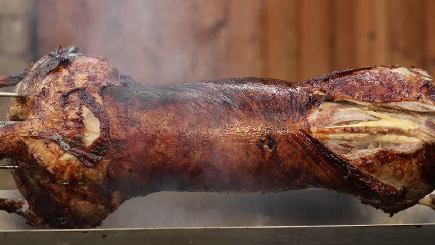 Roasted pig 4K video. A whole pig or lamb being roasted slowly on a metal spit over an open fire, covered in smoke. A traditional way of cooking for festivals or holidays.