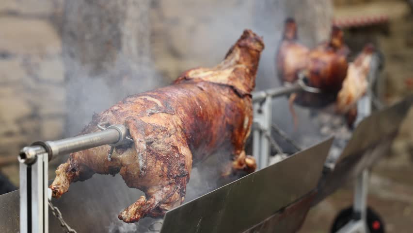 Roasted pig 4K video. A whole pig or lamb being roasted slowly on a metal spit over an open fire, covered in smoke. A traditional way of cooking for festivals or holidays.