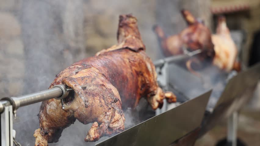 Roasted pig 4K video. A whole pig or lamb being roasted slowly on a metal spit over an open fire, covered in smoke. A traditional way of cooking for festivals or holidays.