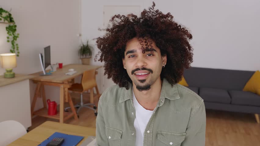 Cheerful portrait of young adult man smiling at camera standing at modern apartment, showcasing a joyful and friendly expression directly at the camera