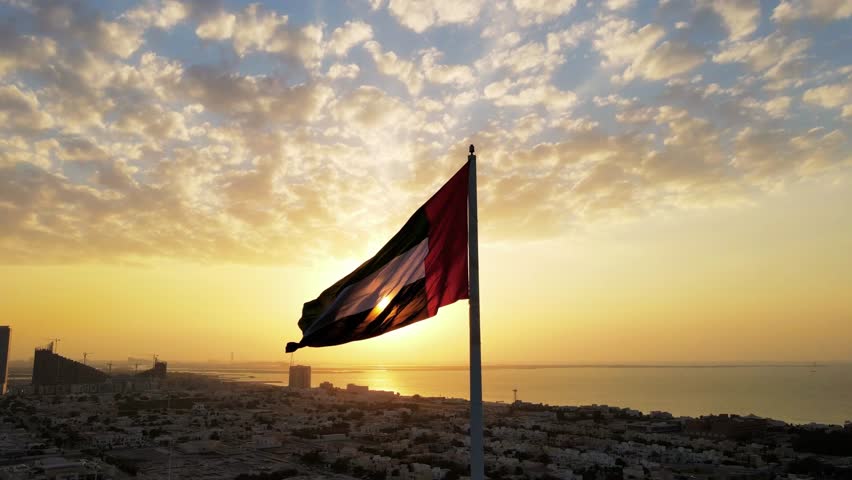 Silhouette of the United Arab Emirates flag waving against the sky with sun in the background, symbolizing patriotism, national pride, and UAE identity.