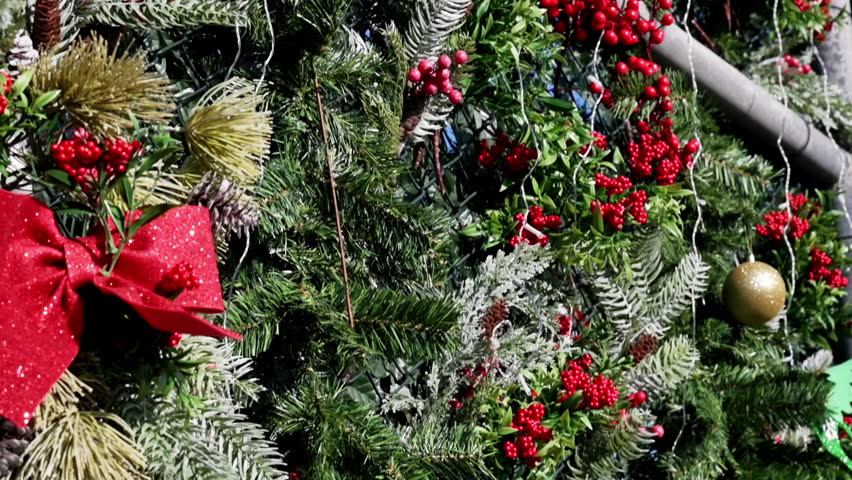 Smooth sliding video shot of a wall decorated with Christmas ornaments, festive greenery, red berries, ribbons, and holiday decorations. Outdoor Christmas atmosphere in natural daylight. Clean seasonal background with rich details, ideal for holiday promotions, New Year advertising, festive designs, and seasonal video projects.