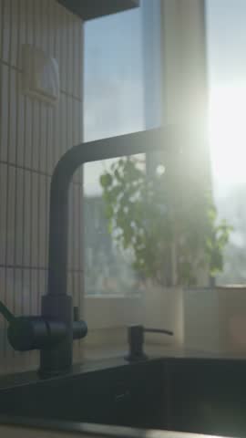 Hand filling glass with drinking water from kitchen faucet in modern home interior. Woman pouring clear water from tap filter. Concept of drinking water, daily hydration and quenching thirst