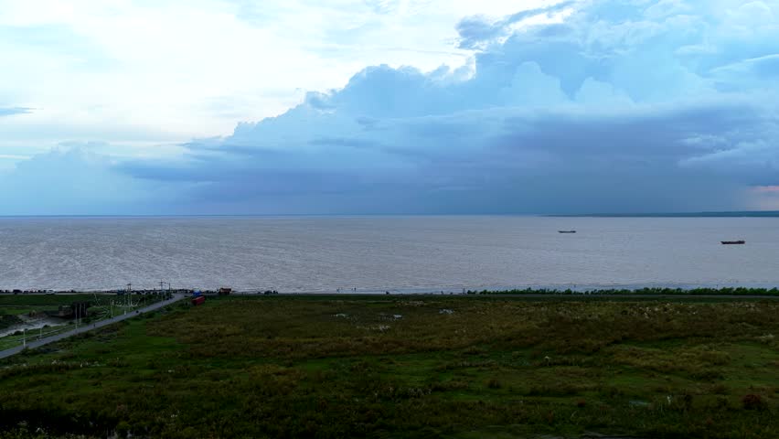 Dramatic storm clouds gathering over a wide expanse of water and grassy shoreline Aerial video