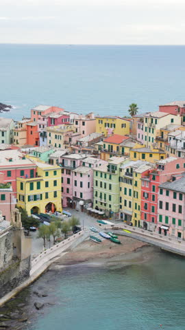 High-angle view of Vernazza harbor in Cinque Terre Italy featuring colorful pastel houses, small fishing boats, curved waterfront promenade and calm Mediterranean Sea, iconic European coastal village