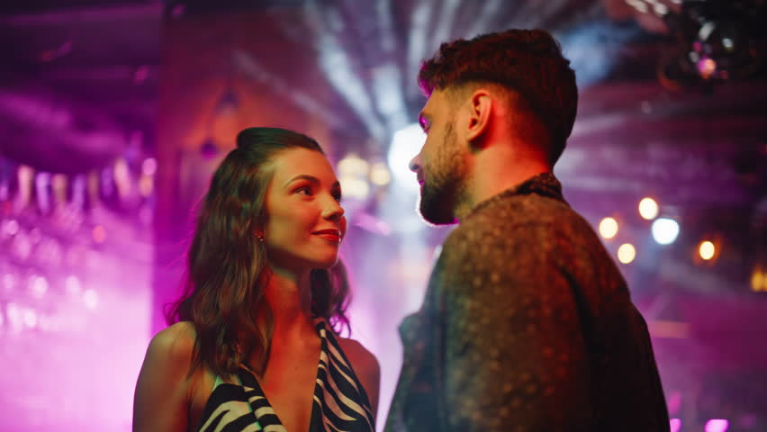 Sweet couple dancing together at bright disco lights closeup. Romantic pair moving at dark dancefloor looking each other with love. Relaxed girlfriend boyfriend enjoying romantic date in night club.