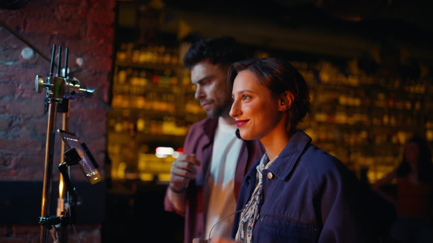 Two people watching concert on screen in dark nightclub. Couple professional videographers filming live performance on stage night rock bar. Smiling operators recording party in club. Show shooting.