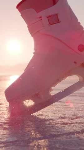 SLOW MOTION, CLOSE UP, LENS FLARE: Ice skater stomps her skate into the ice, kicking up particles glistening in winter evening sunlight. Cinematic shot of woman's ice skates and sparkling snowflakes