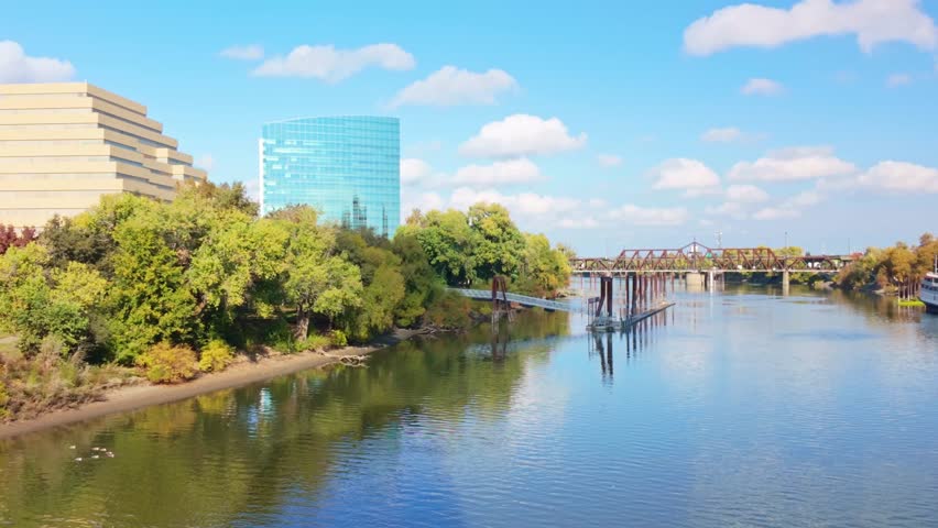 Modern skyscrapers of the Sacramento skyline towering over the green grass and trees of River Walk Park on a bright sunny day