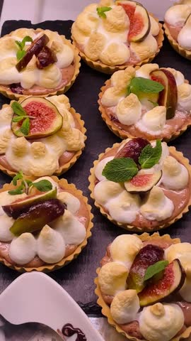 assorted pastry tarts and glazed trays, artisan patisserie display with fig slices, cream dollops, almond garnish, nut crumble, close up bakery counter. Vertical, taken on the mobile device.