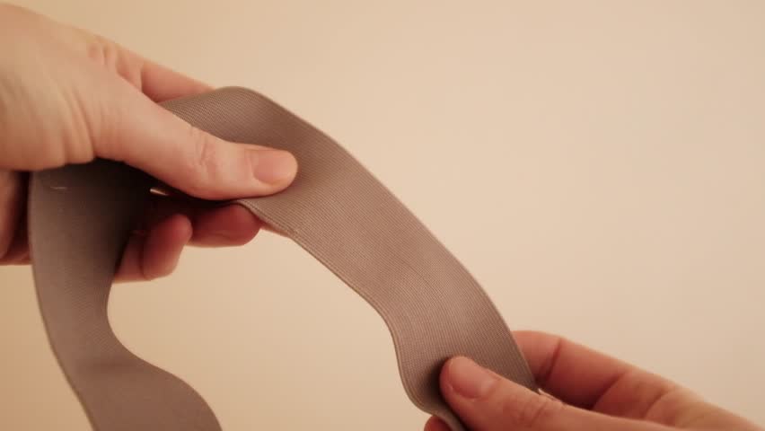Closeup of female hands carefully demonstrates rubber band. Minimal sewing scene, highlighting manual sewing manufacture. Working process in a small business sewing workshop.