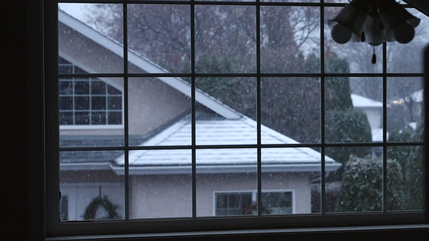 Early snow fall outside, from the point of view of inside a home with a big grid window. View of the neighbour