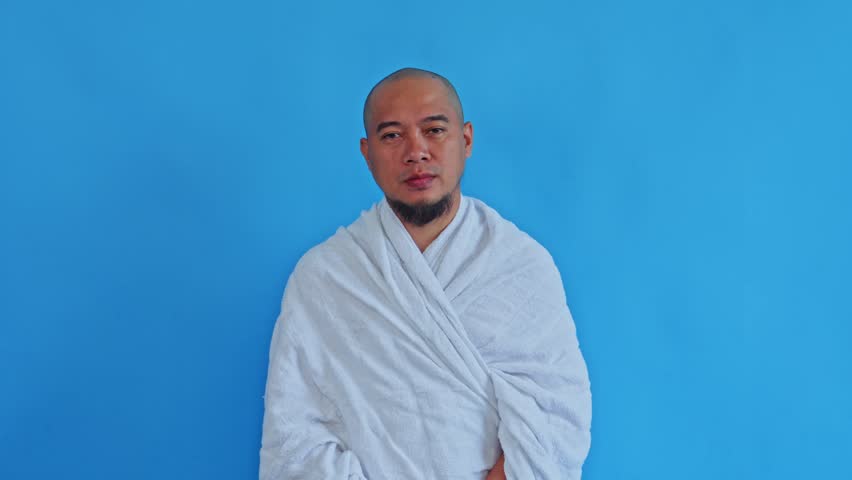 Confused Muslim pilgrim in Ihram garment shrugging with hands open on blue background