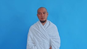Confused Muslim pilgrim in Ihram garment shrugging with hands open on blue background - Powered by Shutterstock - Get 15% off with code: PIKWIZARD15