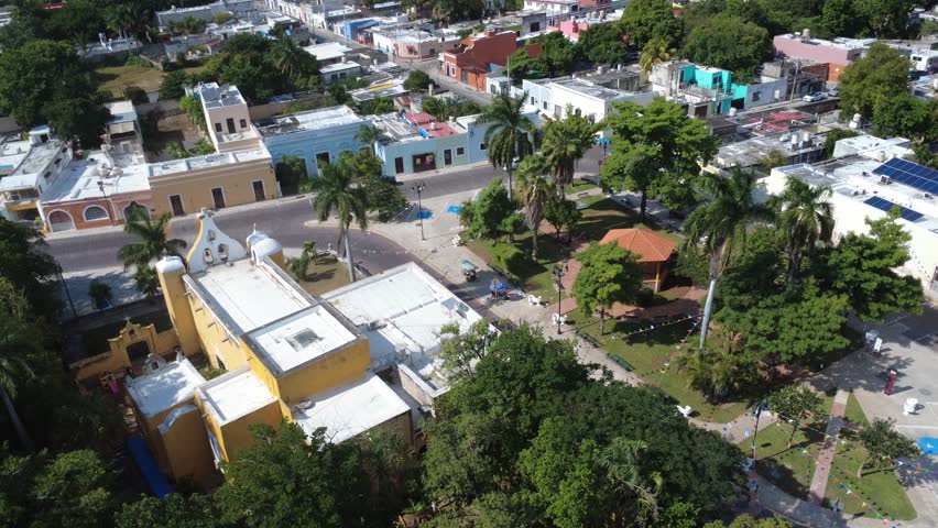 4K drone footage flying over a neighborhood church and public park in Mérida, showing urban greenery, local architecture and everyday life in a traditional Yucatán community.